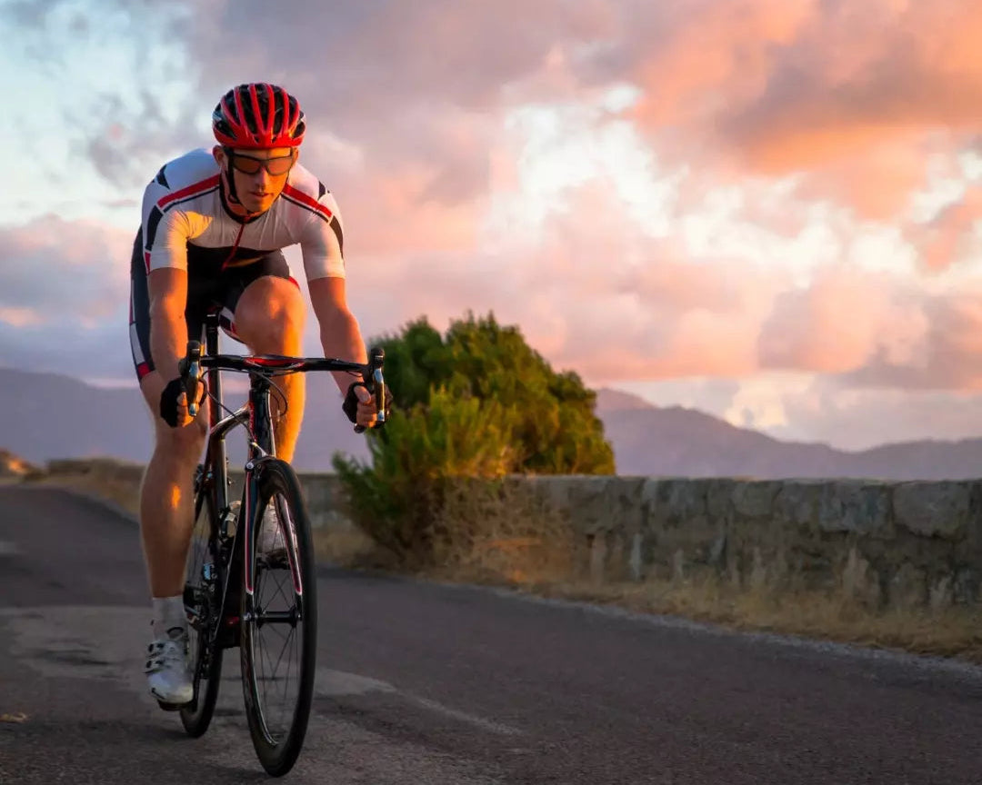 Cyclist riding on a road with a scenic background of mountains and clouds.