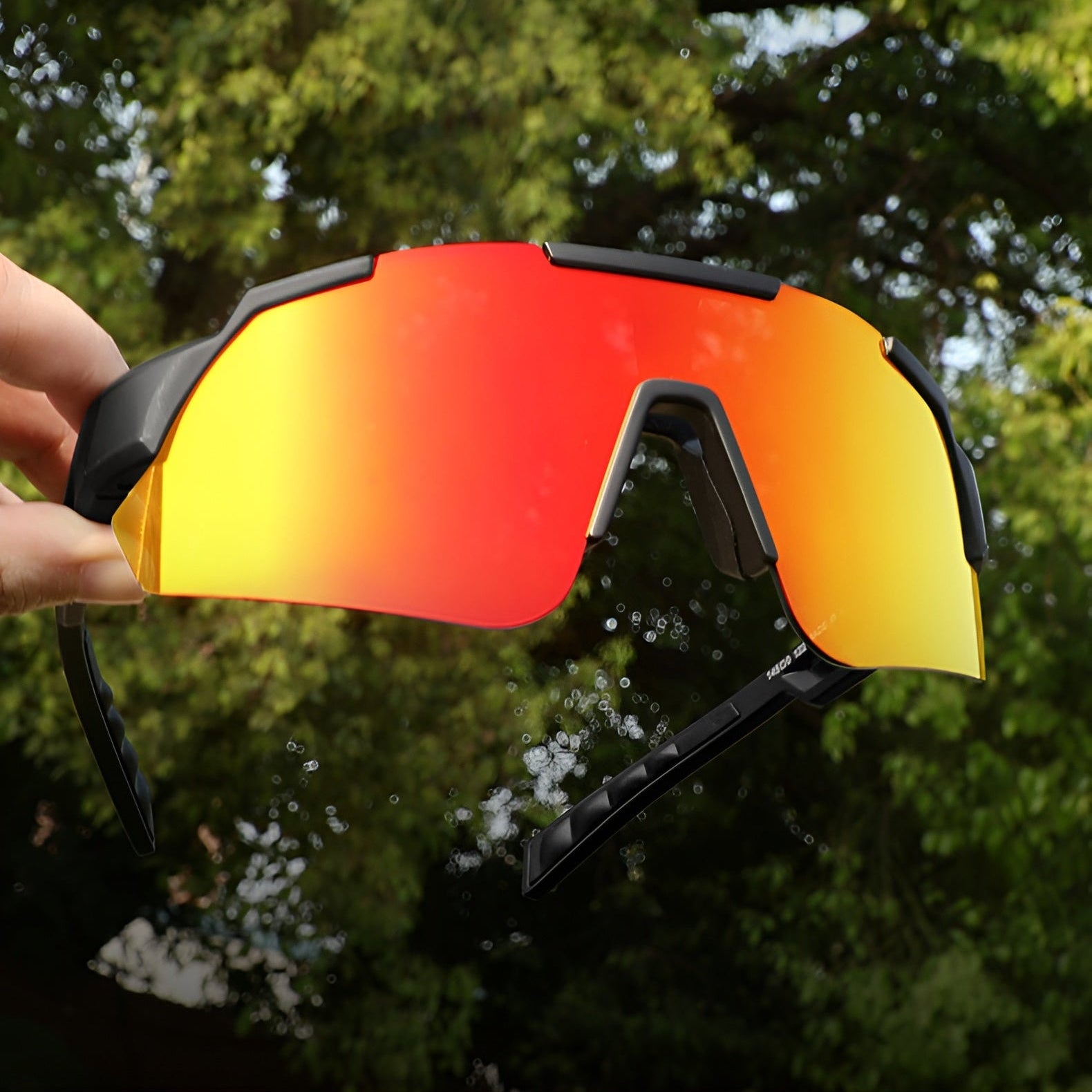 Red and yellow sunglasses held by a hand with green trees in the background